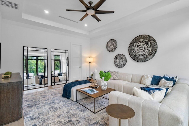 living room with ceiling fan, a tray ceiling, and light wood-type flooring