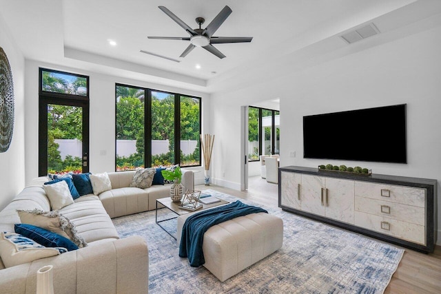 living room featuring ceiling fan, a raised ceiling, and light hardwood / wood-style floors