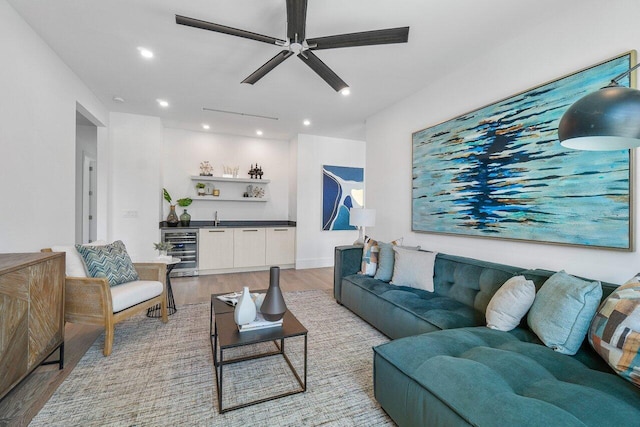 living room featuring ceiling fan, beverage cooler, light hardwood / wood-style floors, and indoor bar