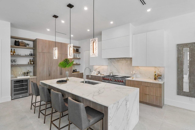 kitchen with wine cooler, white cabinets, double oven range, a kitchen island with sink, and sink