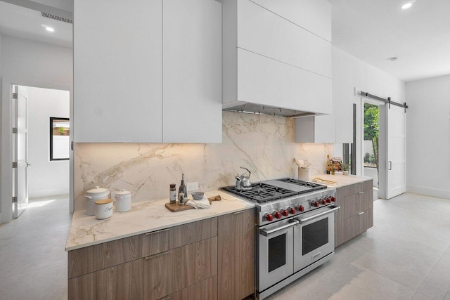 kitchen featuring a barn door, backsplash, white cabinets, and range with two ovens