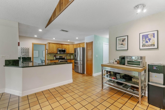 kitchen featuring stainless steel appliances, kitchen peninsula, light tile patterned floors, and a textured ceiling