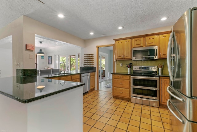 kitchen with light tile patterned flooring, kitchen peninsula, stainless steel appliances, a textured ceiling, and sink