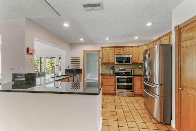 kitchen with light tile patterned floors, sink, kitchen peninsula, a textured ceiling, and appliances with stainless steel finishes