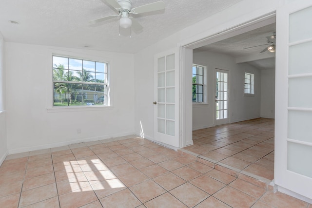 empty room with a textured ceiling, ceiling fan, and light tile patterned floors