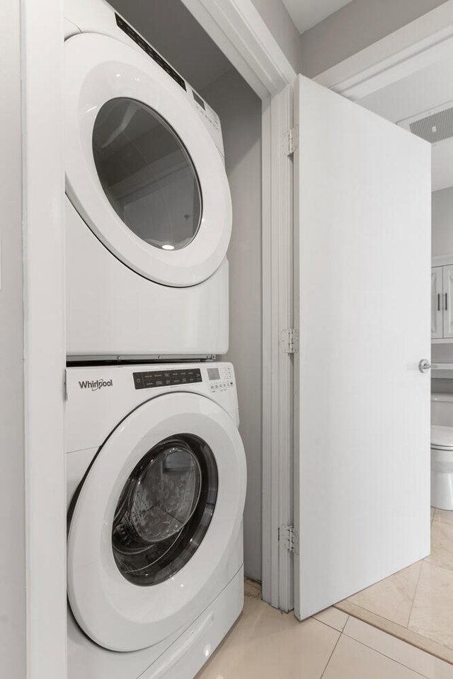 washroom with stacked washer / drying machine and light tile patterned floors