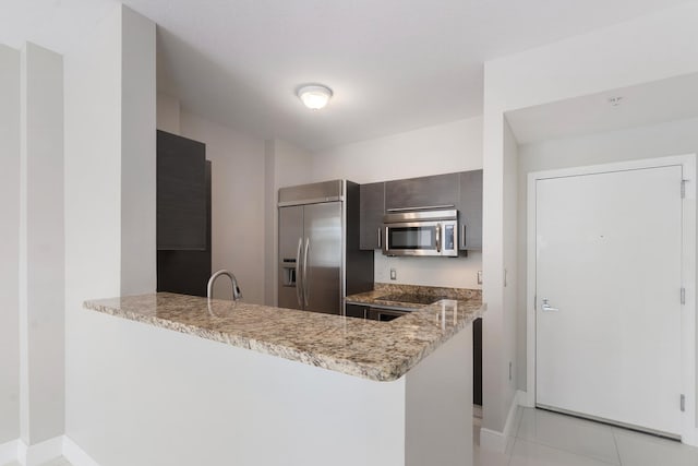 kitchen featuring appliances with stainless steel finishes, light tile patterned flooring, light stone counters, kitchen peninsula, and sink