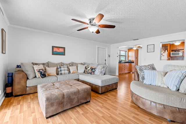 living room featuring light hardwood / wood-style flooring, ceiling fan, ornamental molding, and a textured ceiling