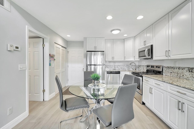 kitchen with sink, appliances with stainless steel finishes, white cabinetry, light stone countertops, and light wood-type flooring