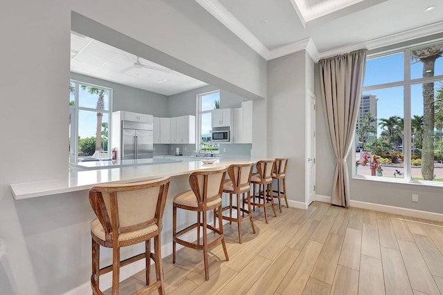 kitchen with sink, a breakfast bar, built in appliances, white cabinets, and kitchen peninsula