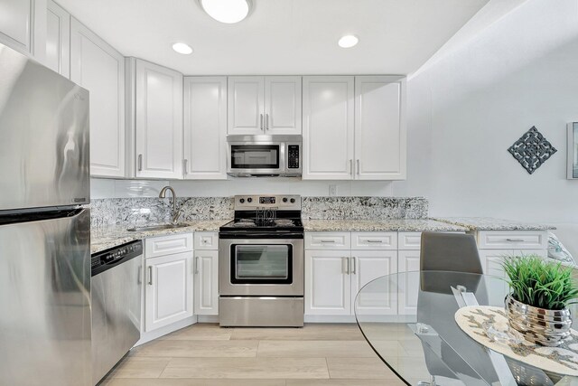 kitchen with sink, stainless steel appliances, white cabinets, and light stone countertops