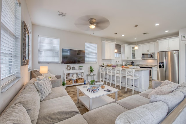 living area with light wood-type flooring, a ceiling fan, visible vents, and recessed lighting