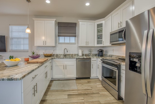 kitchen featuring light wood-type flooring, sink, white cabinets, stainless steel appliances, and decorative light fixtures