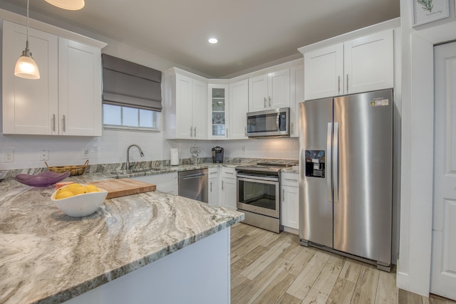 kitchen featuring light wood-type flooring, light stone counters, white cabinetry, appliances with stainless steel finishes, and decorative light fixtures