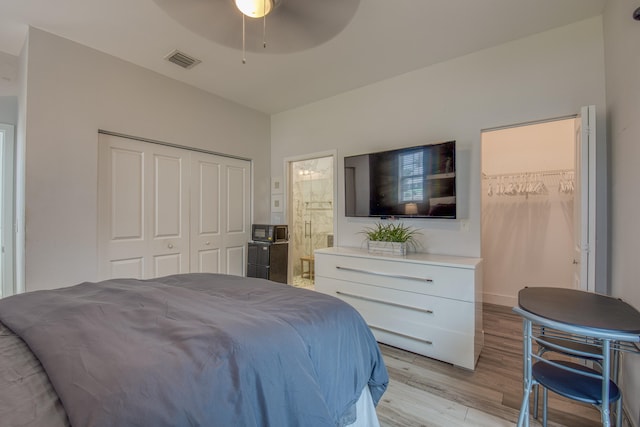 bedroom with light wood-type flooring, connected bathroom, ceiling fan, and a closet