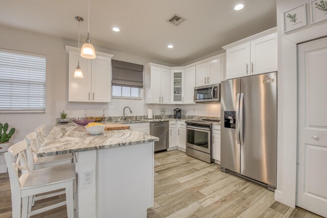 kitchen with light hardwood / wood-style floors, white cabinets, backsplash, pendant lighting, and stainless steel appliances