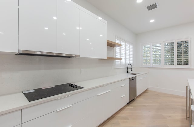 kitchen with light wood-type flooring, stainless steel dishwasher, black electric cooktop, white cabinets, and range hood