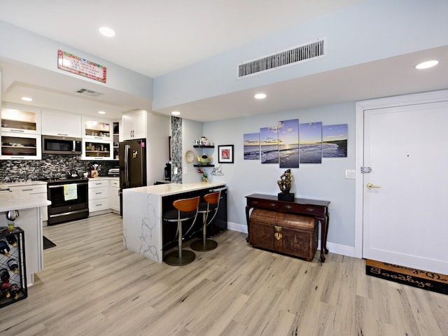 kitchen featuring white cabinetry, a breakfast bar, kitchen peninsula, stainless steel appliances, and light hardwood / wood-style flooring