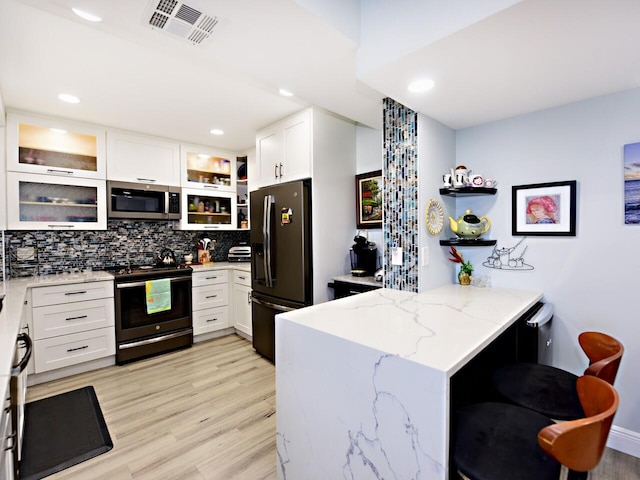 kitchen featuring light stone counters, tasteful backsplash, white cabinets, stainless steel appliances, and light wood-type flooring