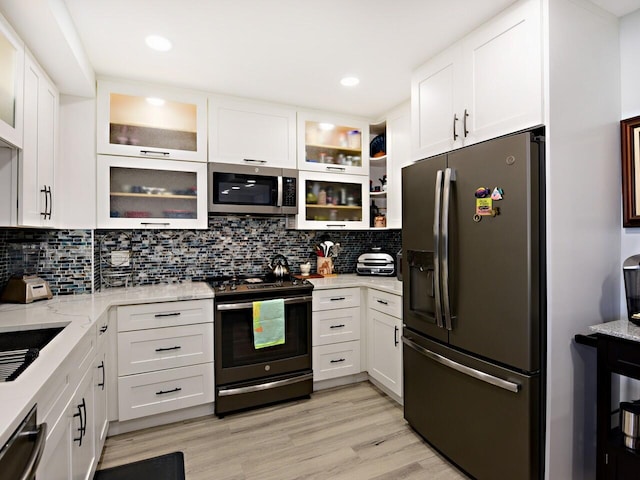 kitchen with light wood-type flooring, light stone counters, white cabinetry, stainless steel appliances, and backsplash