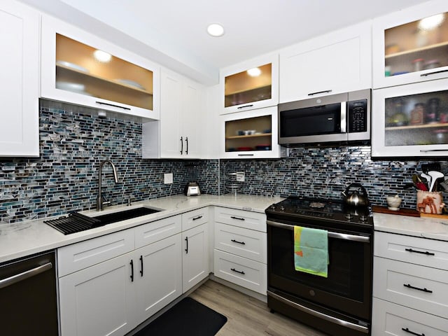 kitchen featuring sink, backsplash, white cabinetry, stainless steel appliances, and light hardwood / wood-style floors