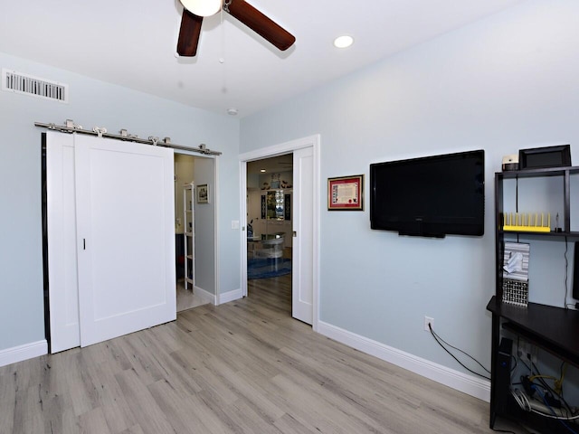 interior space with light hardwood / wood-style floors, ceiling fan, and a barn door