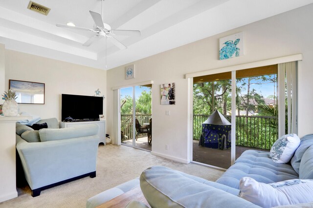 living room with light carpet, a tray ceiling, and ceiling fan