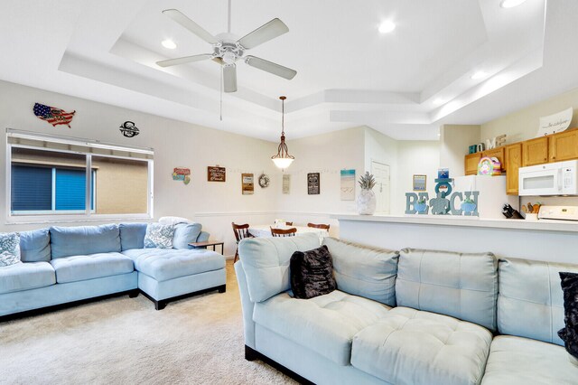 living room featuring a tray ceiling, ceiling fan, and light colored carpet