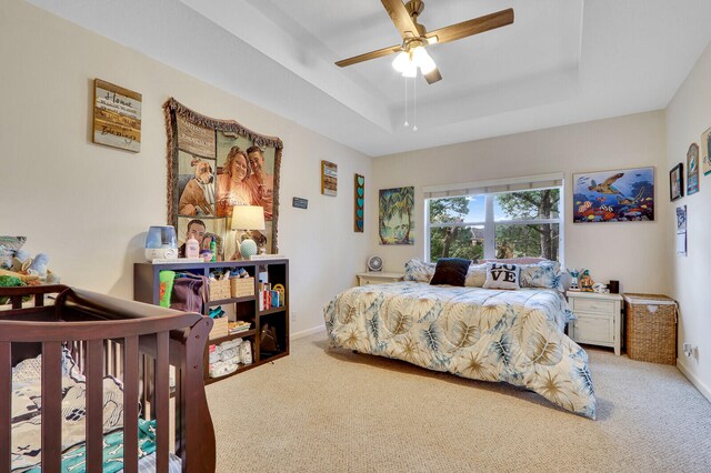 carpeted bedroom with a raised ceiling and ceiling fan