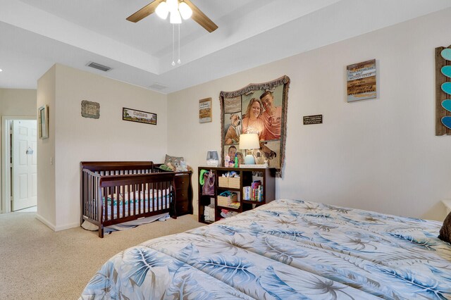 carpeted bedroom with ceiling fan and a tray ceiling