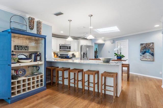 kitchen with white cabinets, a skylight, kitchen peninsula, decorative light fixtures, and appliances with stainless steel finishes