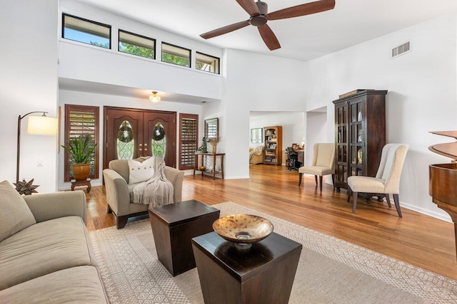 living room with light wood-type flooring, ceiling fan, and a high ceiling