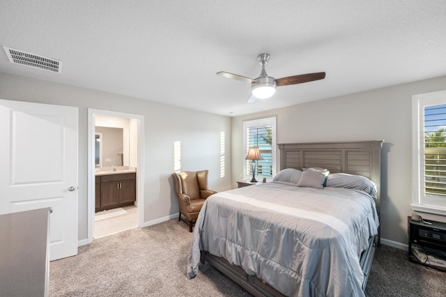 carpeted bedroom with multiple windows, ceiling fan, ensuite bathroom, and a textured ceiling