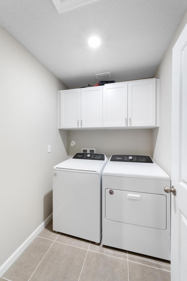 clothes washing area with light tile patterned flooring, cabinets, a textured ceiling, and independent washer and dryer