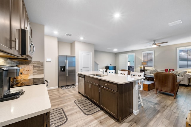 kitchen featuring a kitchen island with sink, sink, light hardwood / wood-style flooring, appliances with stainless steel finishes, and dark brown cabinetry