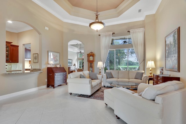 living room featuring a tray ceiling, sink, light tile patterned floors, ornamental molding, and a high ceiling