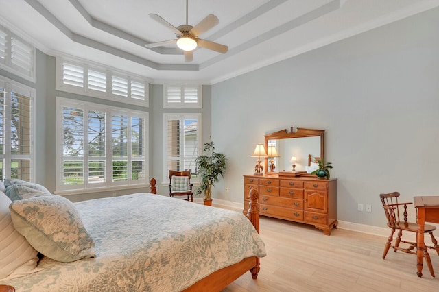 bedroom with ceiling fan, a towering ceiling, a raised ceiling, light wood-type flooring, and crown molding