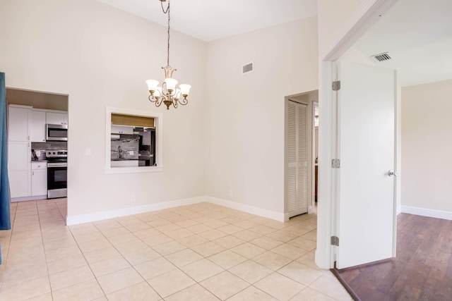 empty room with light tile patterned floors, a chandelier, and a high ceiling