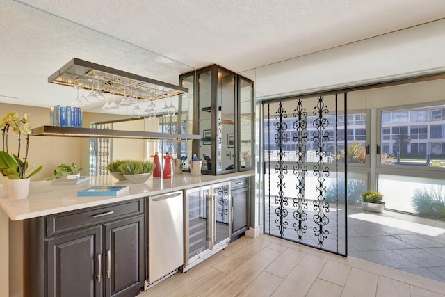 kitchen with a textured ceiling, dark brown cabinets, light hardwood / wood-style floors, wine cooler, and stainless steel refrigerator