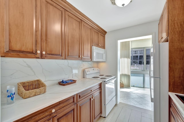 kitchen with backsplash, light stone countertops, white appliances, and light tile patterned floors