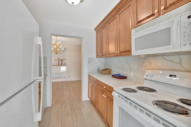 kitchen with white appliances, light wood-type flooring, backsplash, light stone counters, and an inviting chandelier