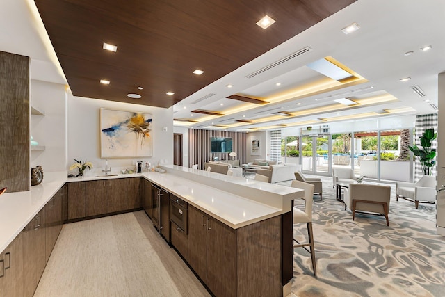 kitchen featuring kitchen peninsula, a breakfast bar area, dark brown cabinets, sink, and light carpet