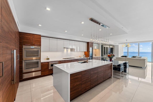 kitchen featuring appliances with stainless steel finishes, a water view, an island with sink, white cabinets, and decorative light fixtures