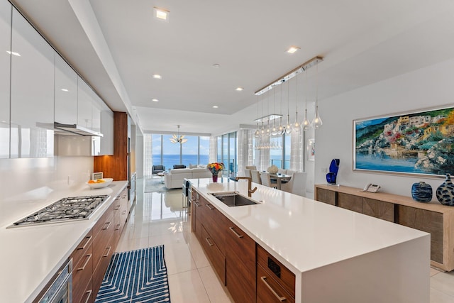 kitchen with white cabinets, an island with sink, sink, light tile patterned floors, and an inviting chandelier