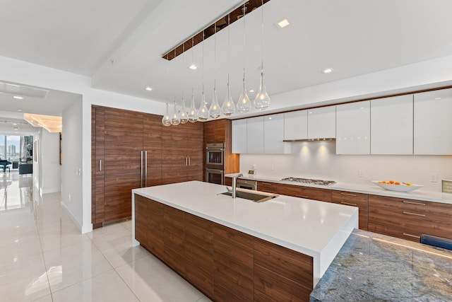 kitchen with an island with sink, white cabinets, stainless steel appliances, decorative light fixtures, and sink