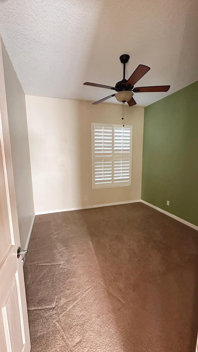 spare room with a textured ceiling, dark carpet, and ceiling fan