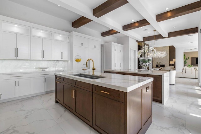 kitchen featuring white cabinets, sink, an island with sink, and beam ceiling