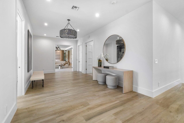 hall with light wood-type flooring and an inviting chandelier