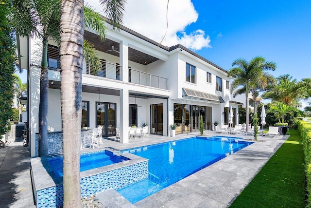 rear view of property with a swimming pool with hot tub, a balcony, and a patio area