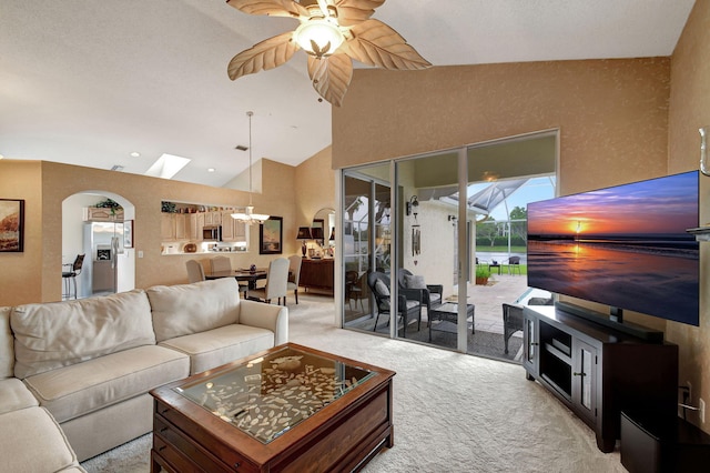 carpeted living room with ceiling fan, a skylight, and high vaulted ceiling